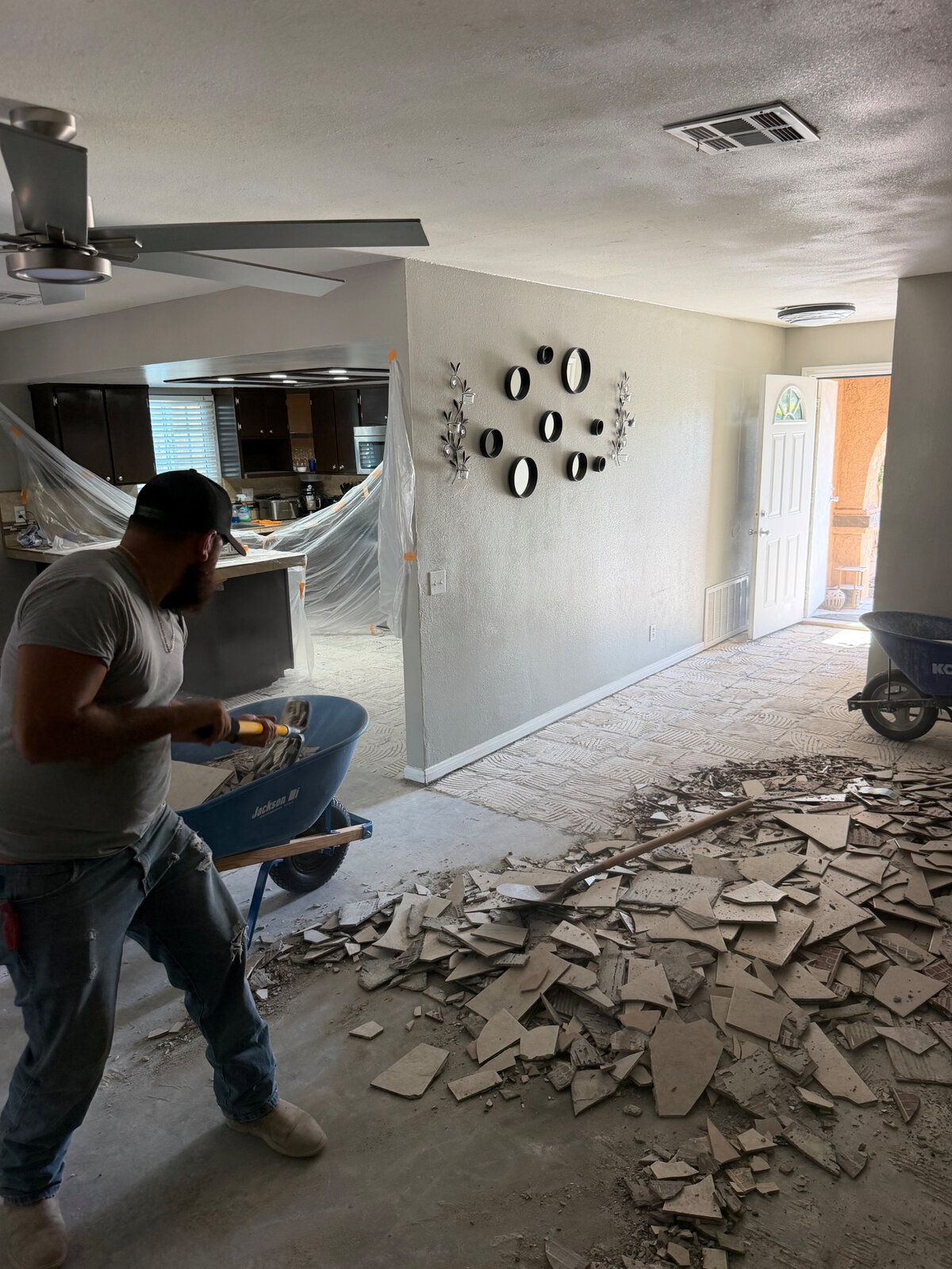 HG Junk Removal crew shoveling removed tile into a wheelbarrow during a demolition cleanup